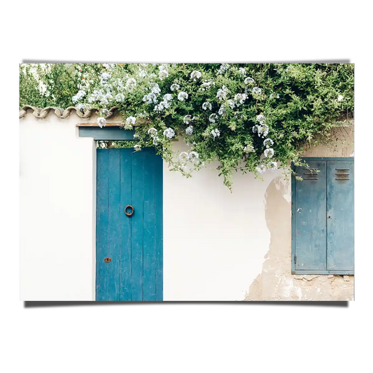 Traditional Greek House Facade with Blue Door and White Flowers in a Sunny Day